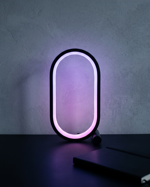 Capsule Lamp lit violet on a dark desk