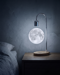 Moon Lamp floating above its wood base on a bedside table in a dark bedroom