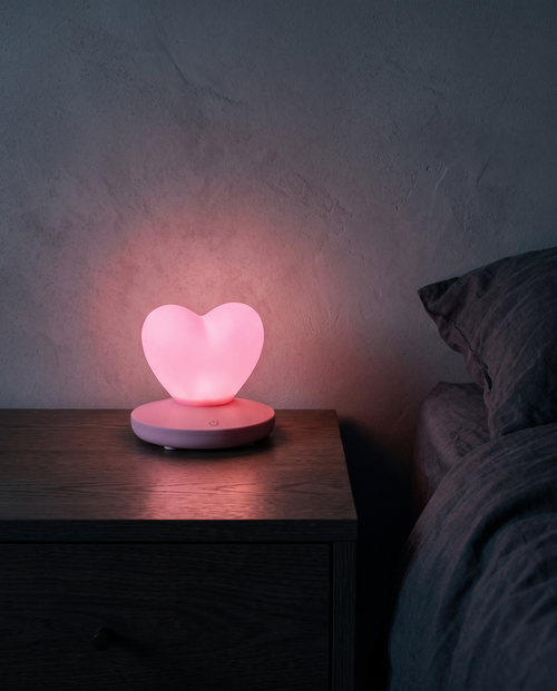 Heart Lamp glowing pink on a bedside table