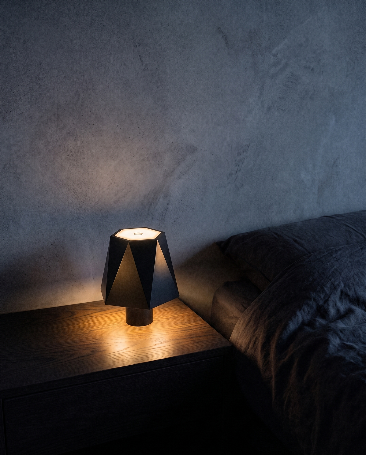 Cordless Table Lamp in black with a faceted shade, lit on a bedside table