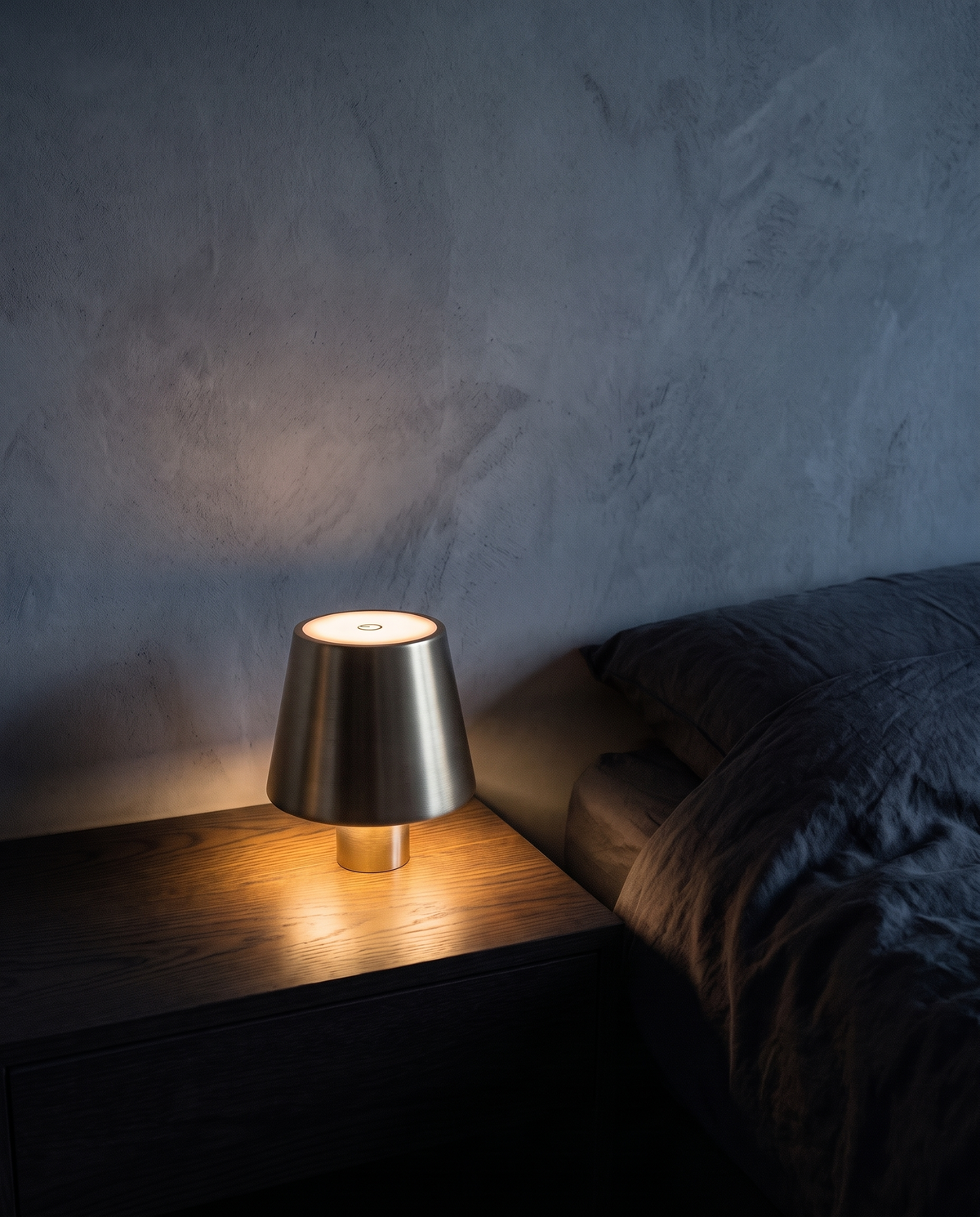 Cordless Table Lamp in gold with a smooth shade, lit on a bedside table