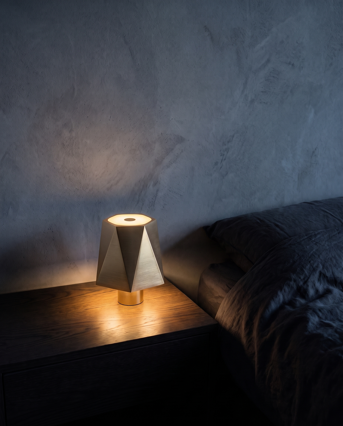 Cordless Table Lamp in gold with a faceted shade, lit on a bedside table
