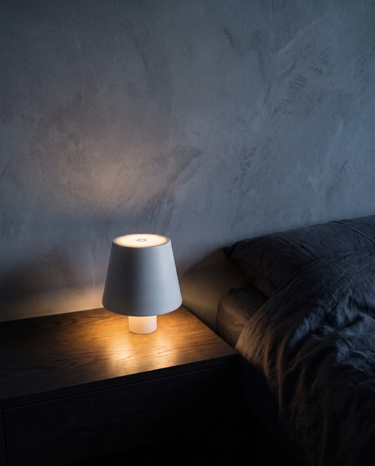 Cordless Table Lamp in white with a smooth shade, lit on a bedside table