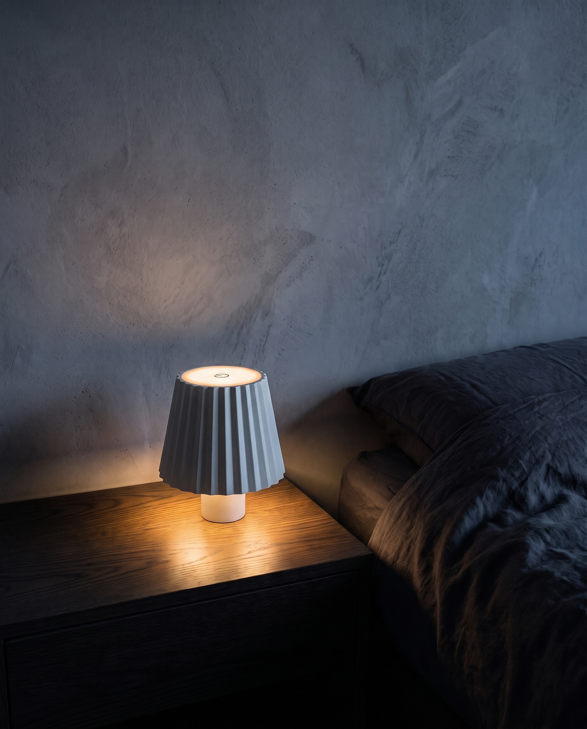 Cordless Table Lamp in white with a pleated shade, lit on a bedside table