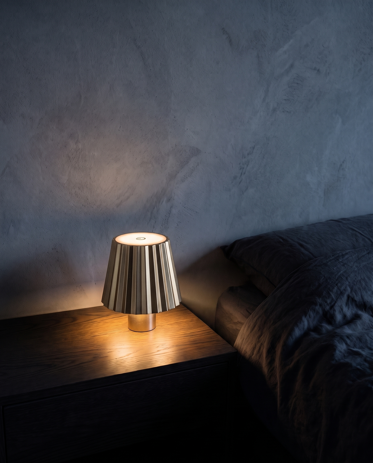 Cordless Table Lamp in gold with a pleated shade, lit on a bedside table