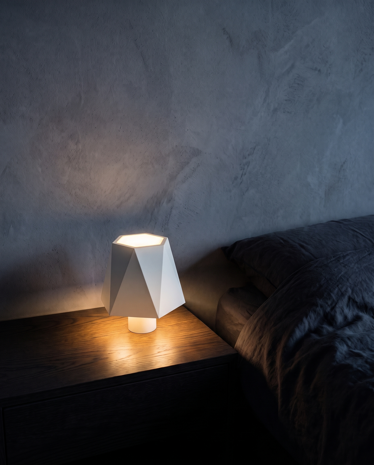 Cordless Table Lamp in white with a faceted shade, lit on a bedside table