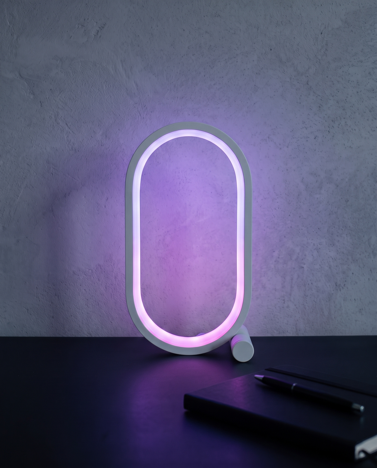 Capsule Lamp in white, lit violet on a dark desk